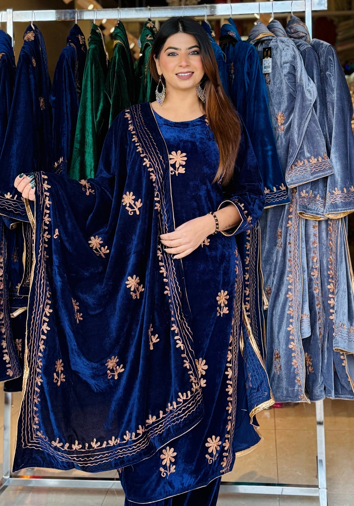 Woman wearing a blue embroidered traditional outfit in front of hanging garments.